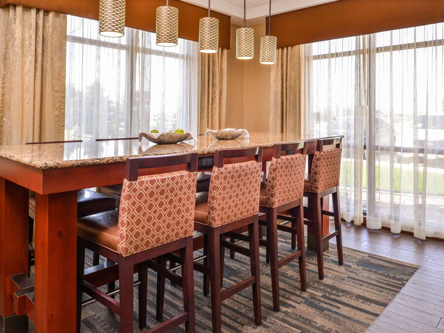 Un espace repas avec une longue table en bois et des chaises assorties, de grandes fenêtres ornées de rideaux légers et des luminaires suspendus en fibres tressées.