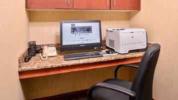 A hotel desk with a desktop computer, a printer, a telephone, and a chair.