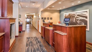 Zona de recepción de un hotel con un largo pasillo, mostradores de madera y un quiosco digital, además de un cartel grande que dice 'explore'.