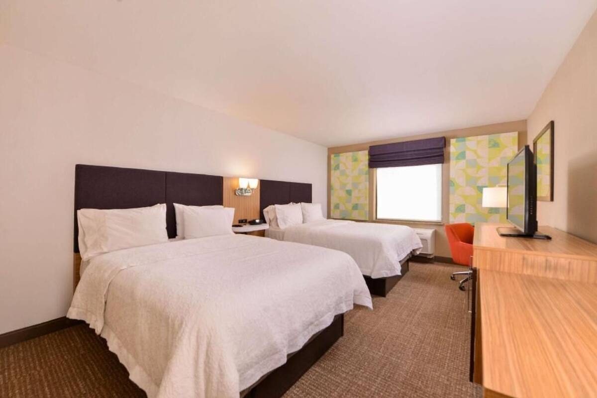 A hotel room with two beds, a desk, a chair, a TV, and a window with a view.