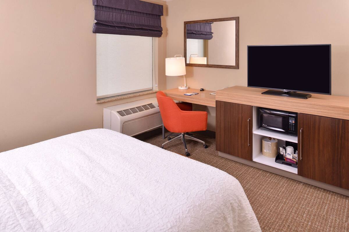 A hotel room with a bed, a desk with a computer, a TV, a microwave, and a chair.