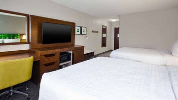Una habitación de hotel con dos camas, un escritorio con silla, un televisor y un microondas.