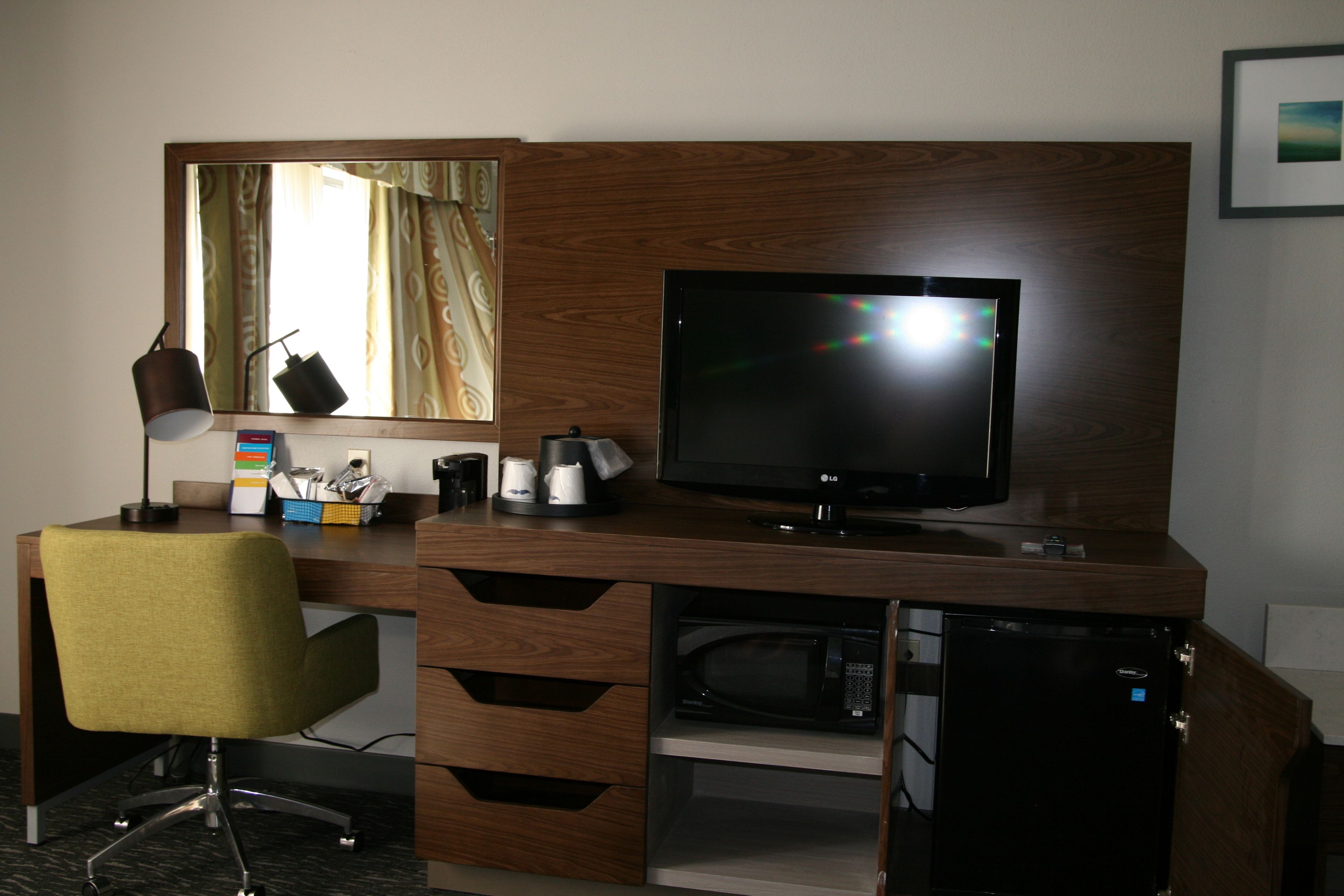 A hotel room with a wooden desk, a television, a microwave, and a chair.