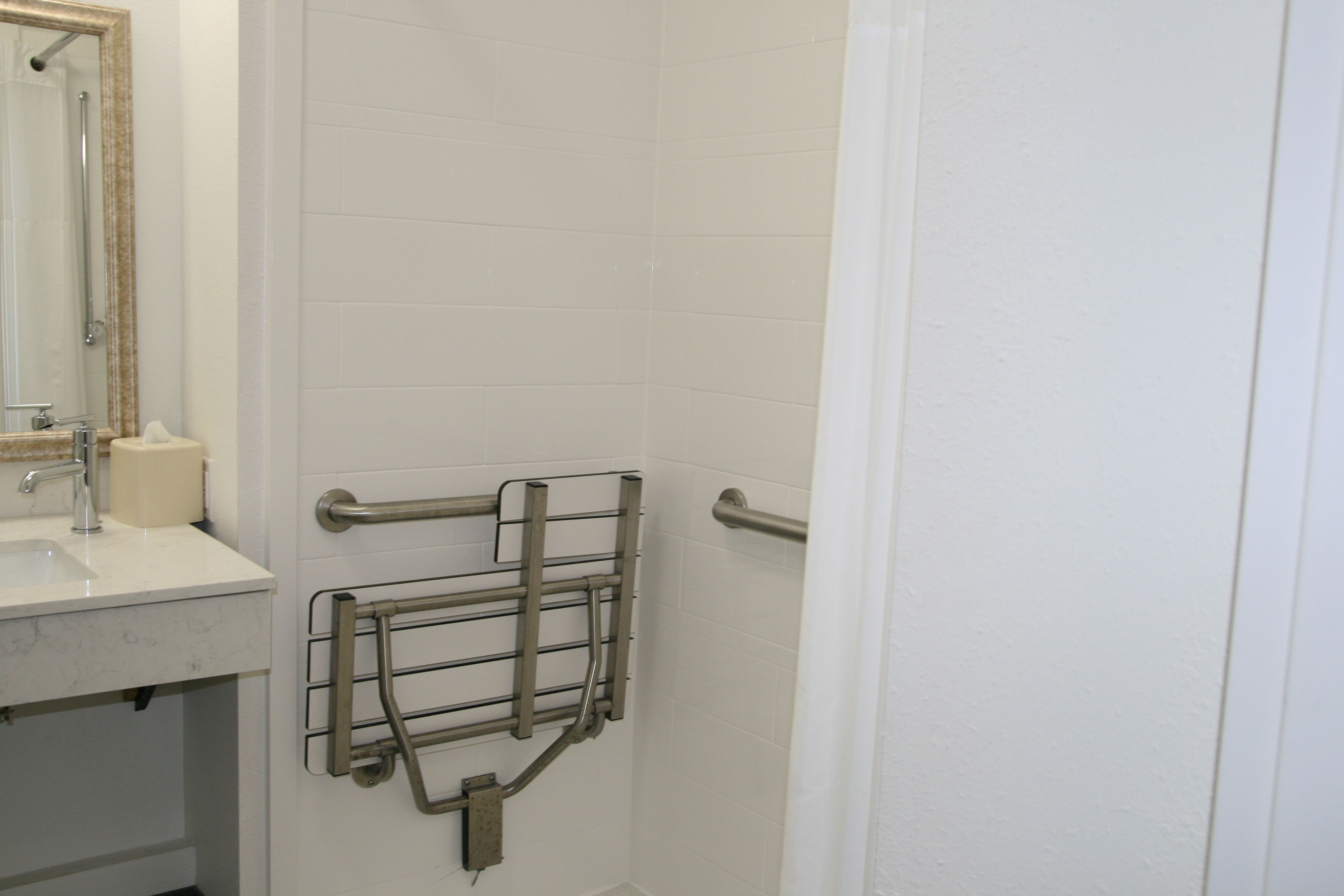 A bathroom with a white sink, a mirror, and a handrail.