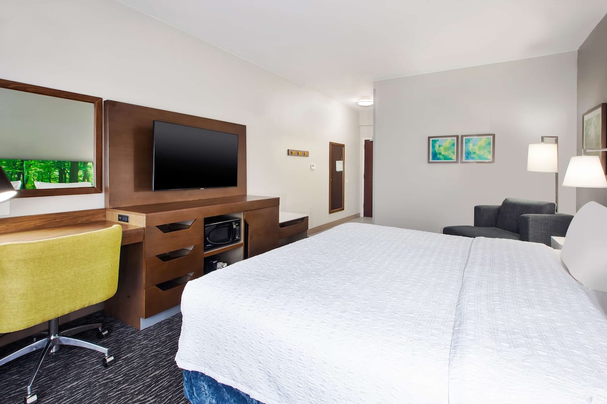 A hotel room with a large bed, a desk with a chair, a flat-screen TV, a microwave, and a lamp.