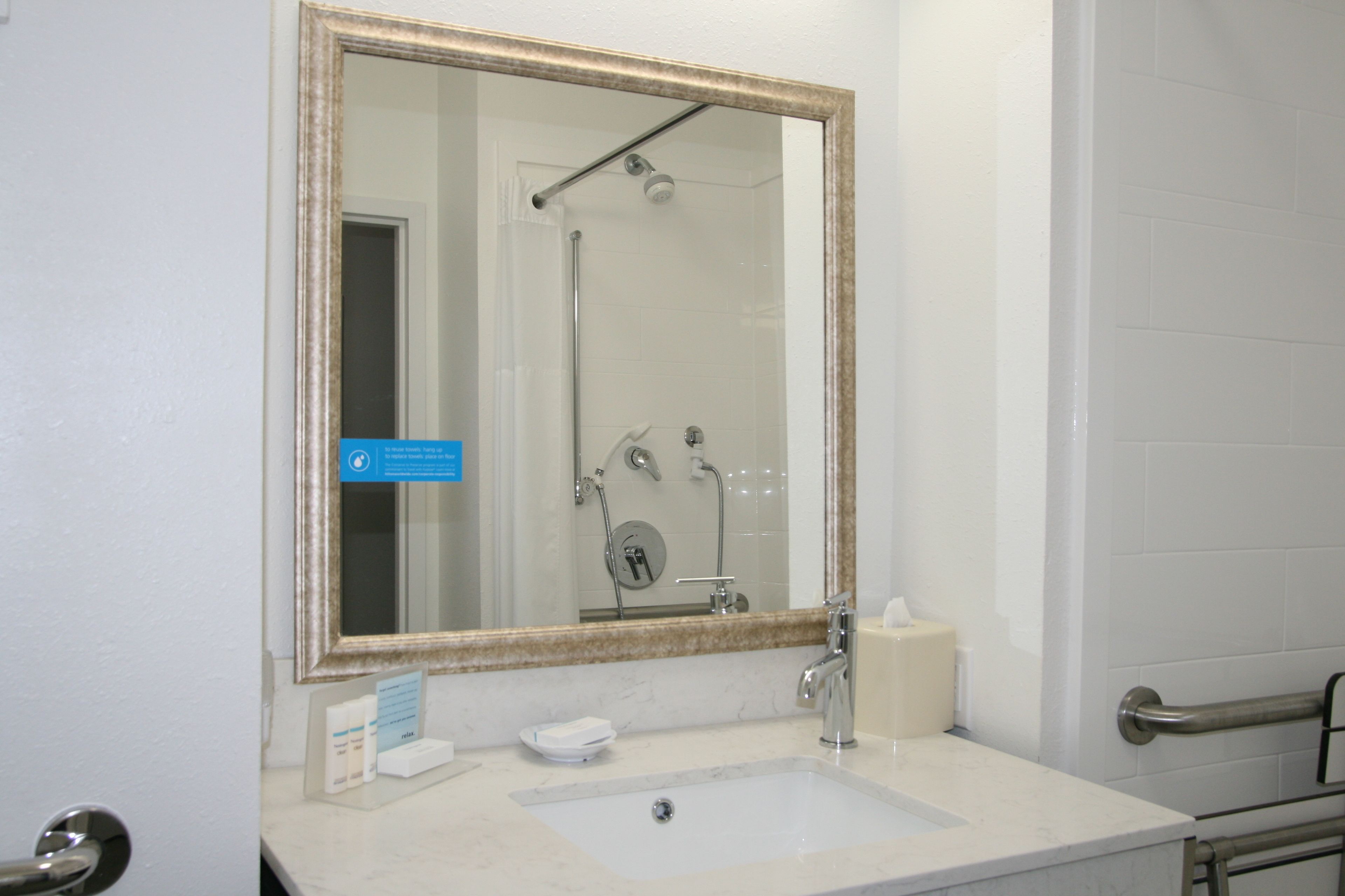 Une salle de bain avec un grand miroir, un lavabo, une serviette et une douche.