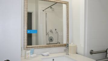 Een badkamer met een grote spiegel, een wastafel, een handdoek en een douche.