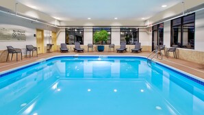 Una piscina interior con agua azul cristalina, rodeada de sillas de descanso y una planta en maceta.