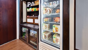Un expositor refrigerado con diferentes alimentos, un estante con aperitivos y un anuncio de megafonía en la parte superior.