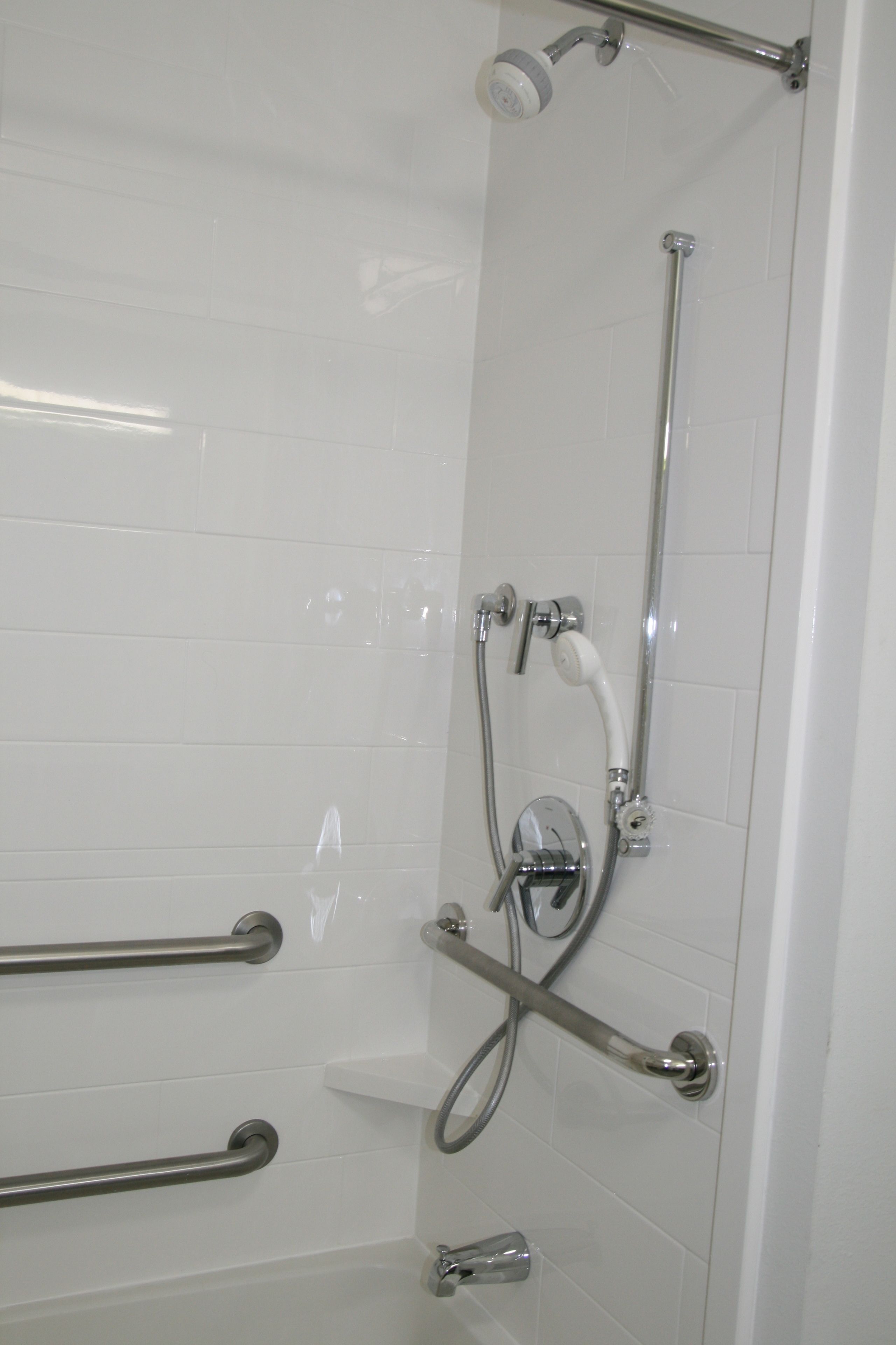 Een douchegedeelte met een glazen deur, een handdouche, een handdouche en een doucheaansluiting.