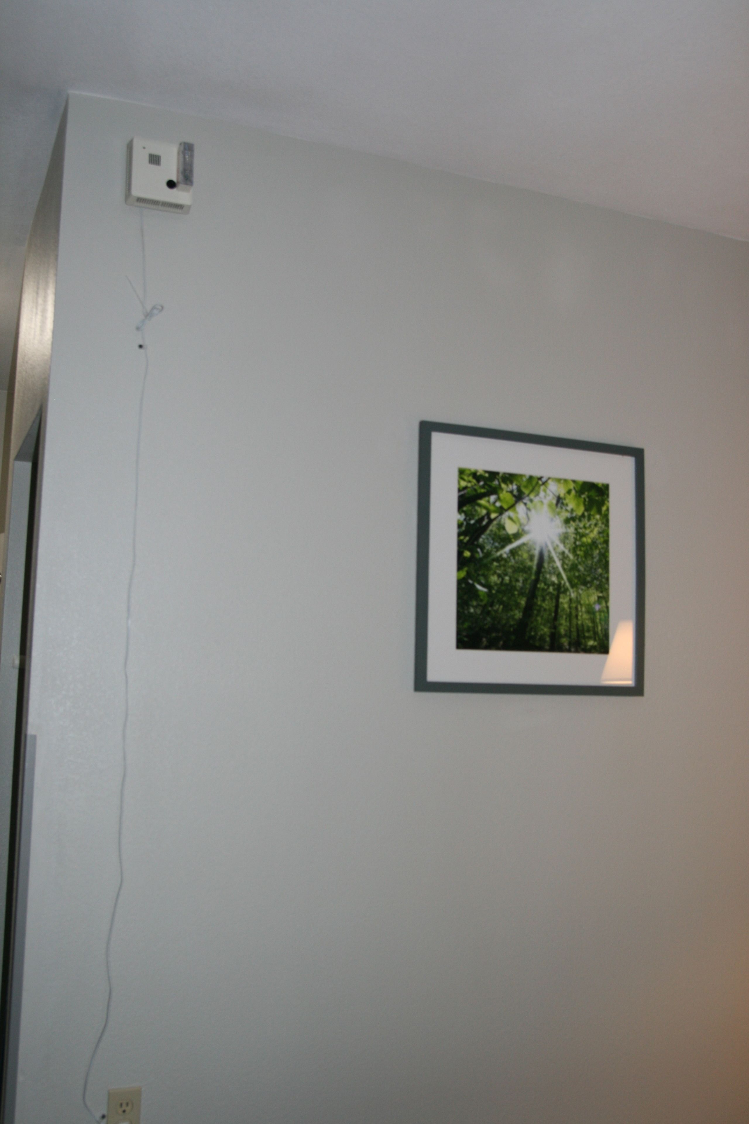 Un cuadro colgado en la pared con un paisaje forestal, un enchufe y un cable.