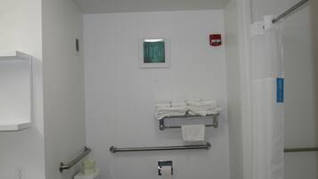 Un baño con inodoro, barra para toallas, pasamanos y detector de incendios.