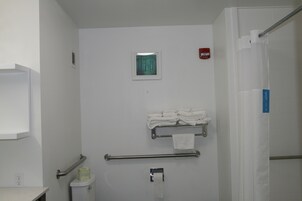 Un baño con inodoro, barra para toallas, pasamanos y detector de incendios.