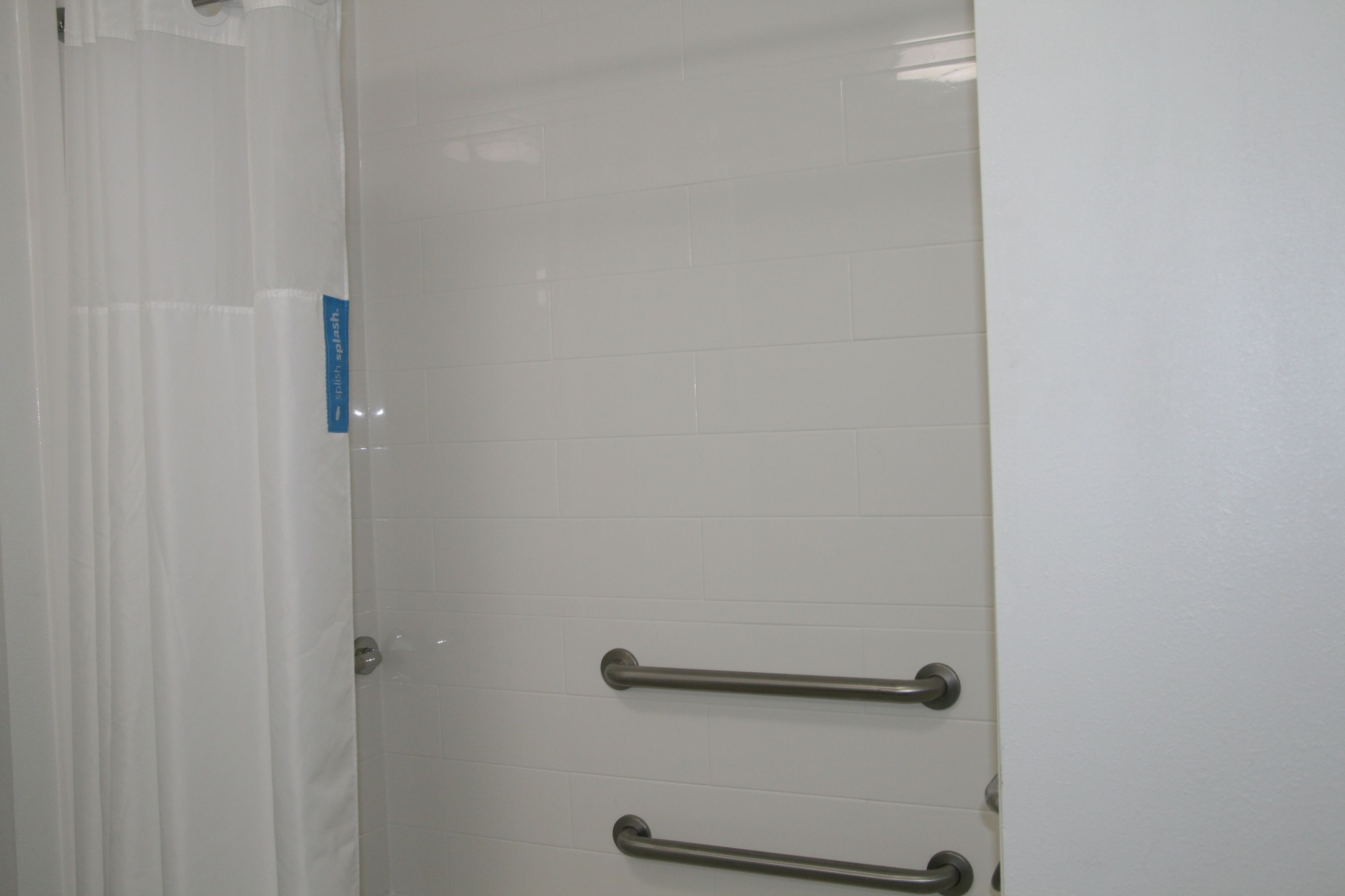 Baño con paredes de azulejos blancos, una puerta blanca y dos barras de metal.