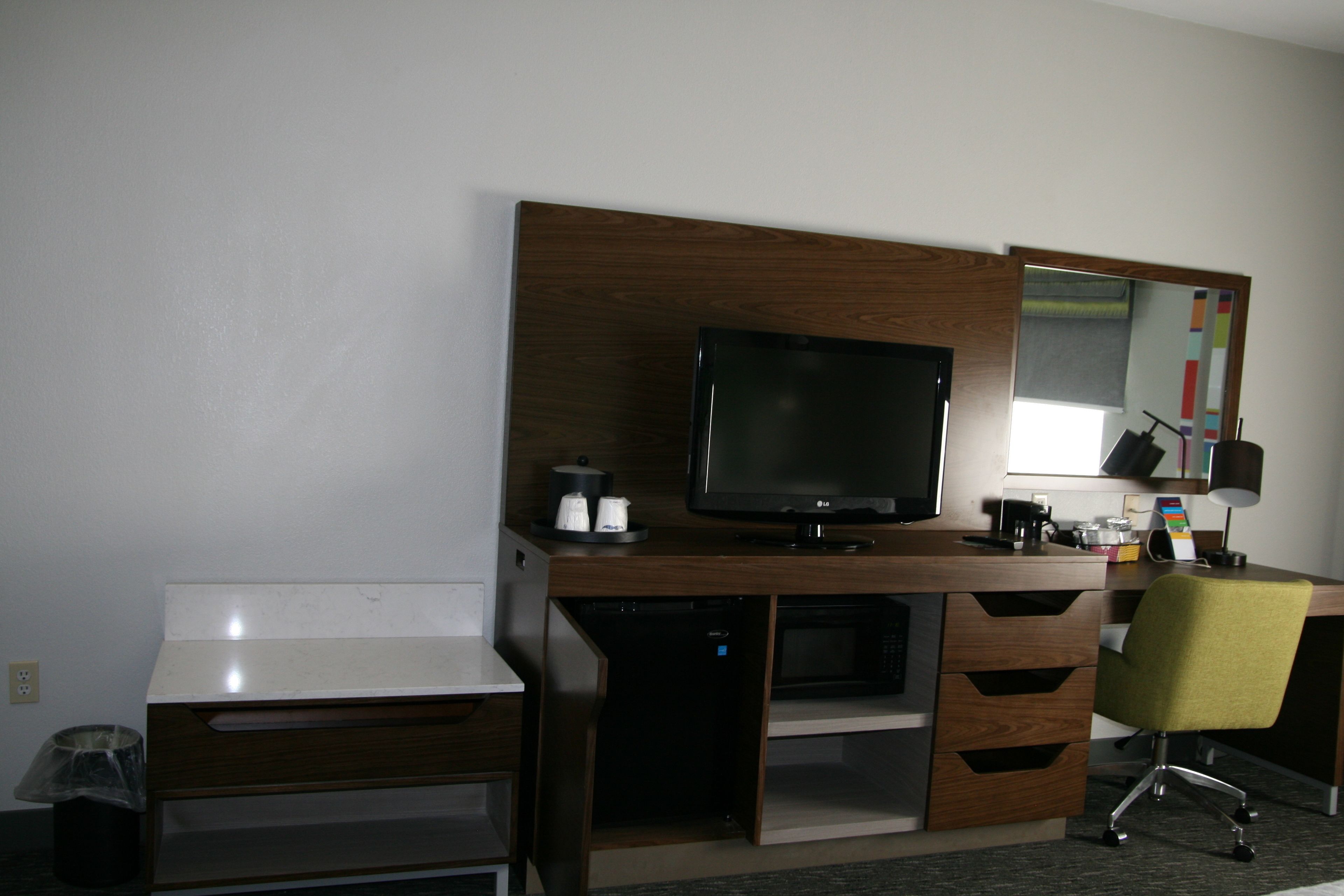 Una habitación de hotel con un escritorio de madera, un televisor, una silla y un espejo.