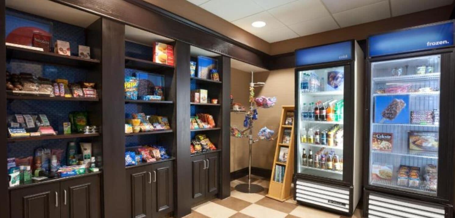 A self-service snack and beverage area with shelves stocked with snacks, a beverage cooler, and a freezer.