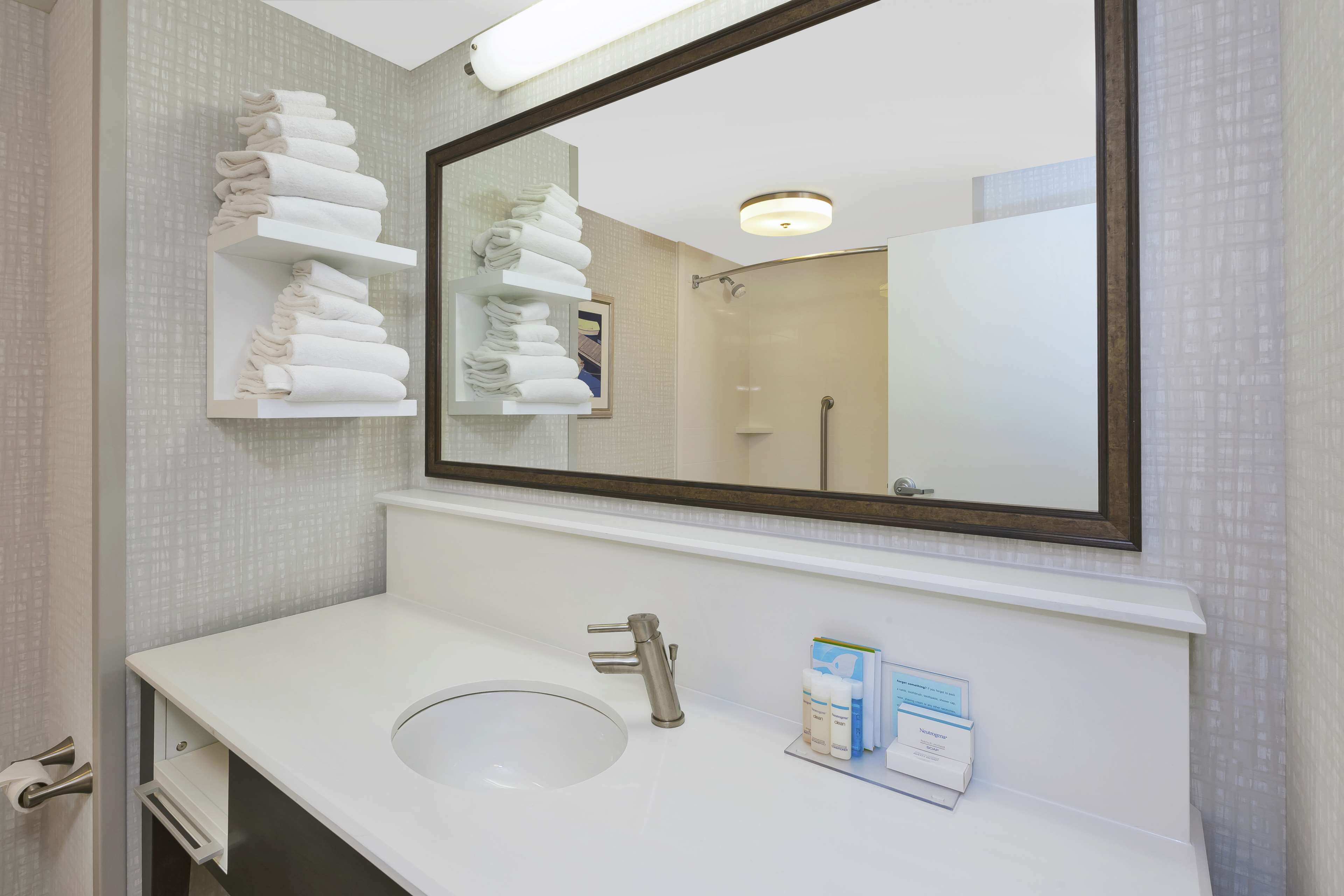 A bathroom with a white sink, a large mirror, and shelves with folded towels.