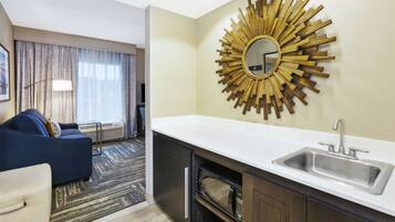A hotel room with a kitchenette, a large mirror, and a sofa.