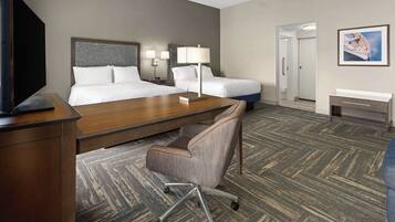 A hotel room with two beds, a desk, a chair, a TV, and a painting on the wall.