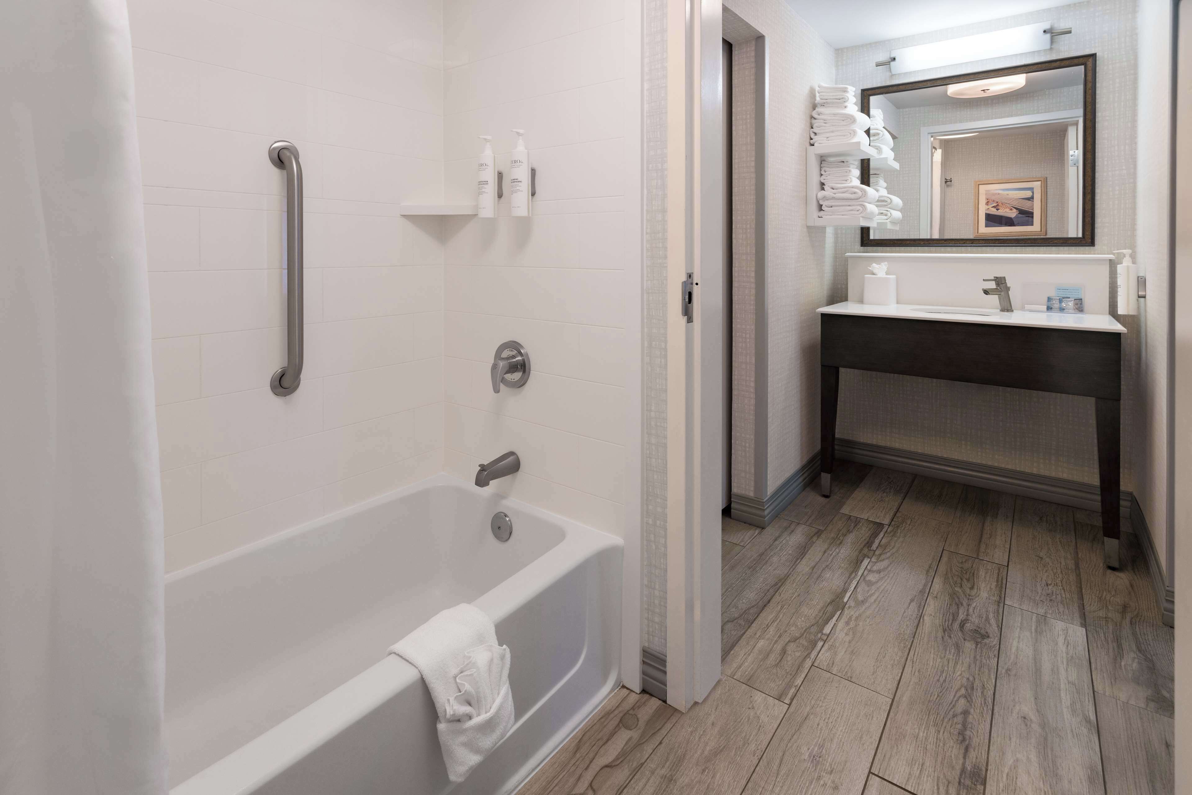 Un bagno moderno con una vasca, un sostegno, un lavandino con specchio e asciugamani ordinatamente disposti.