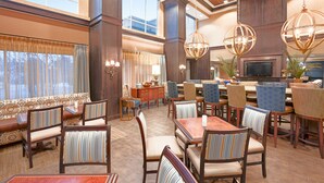 A spacious dining area with high ceilings, large windows, and a variety of seating options including tables and chairs. - Hampton Inn & Suites Wells-Ogunquit (Wells)