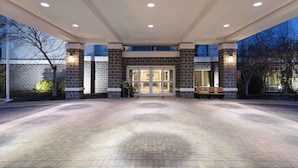 A hotel entrance with a brick facade, a covered walkway, and a bench. - Hampton Inn & Suites Wells-Ogunquit (Wells)