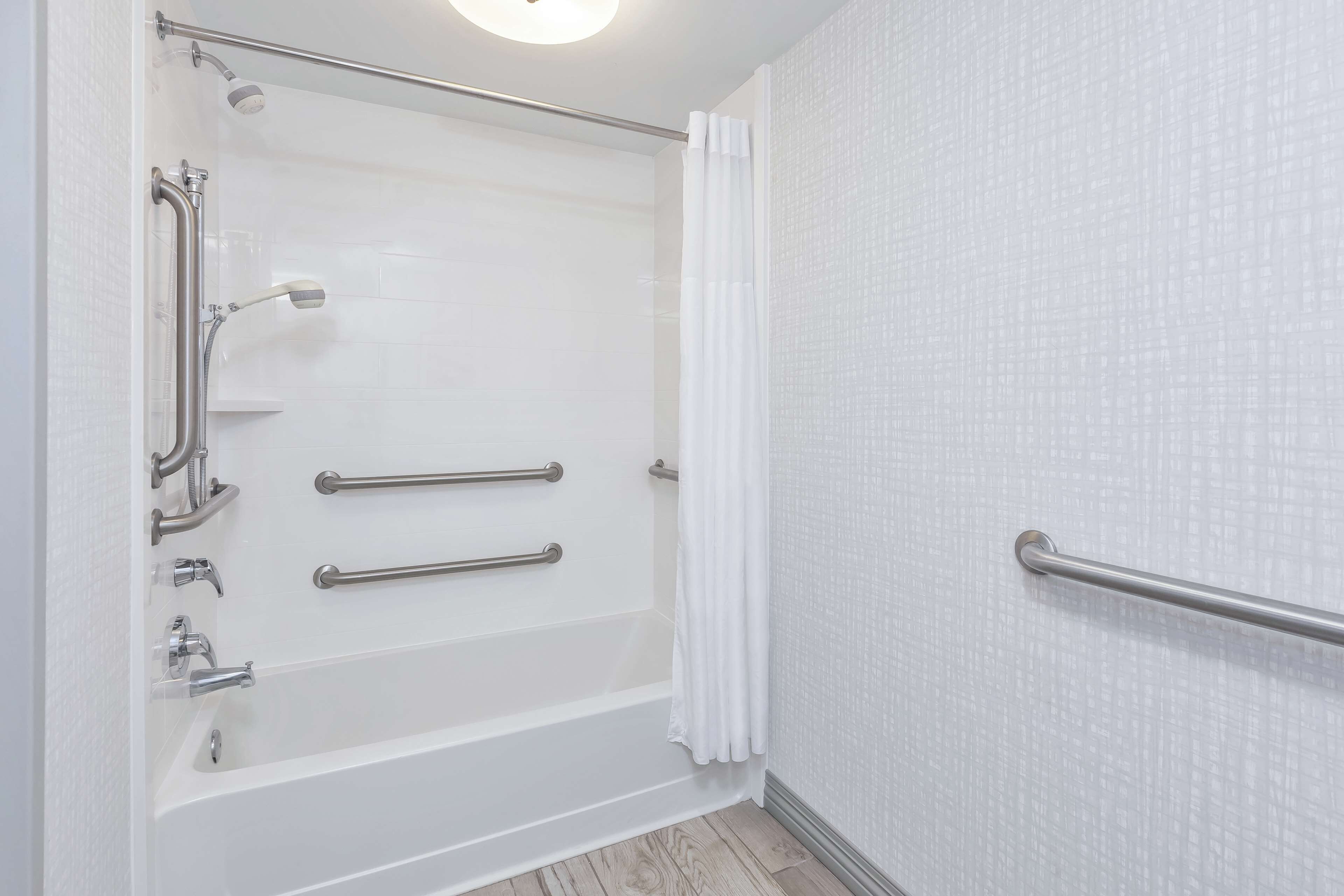 A bathroom with a walk-in shower, grab bars, and a white tiled wall.