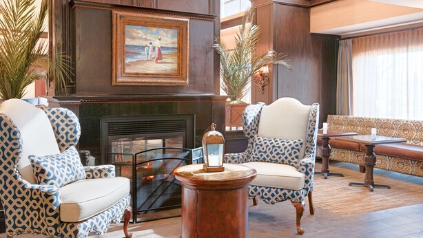 A lobby with a fireplace, patterned chairs, a round table, and a large painting on the wall. - Hampton Inn & Suites Wells-Ogunquit (Wells)