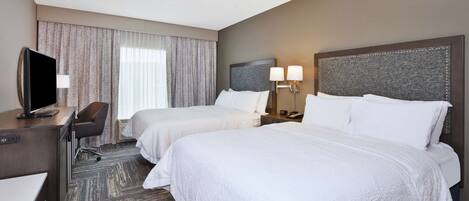 A hotel room with two beds, a desk with a computer, a chair, and a TV.
