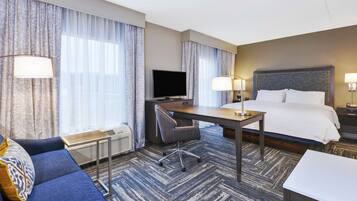 Una habitación de hotel con una cama, un escritorio con una silla, un televisor y un sofá.