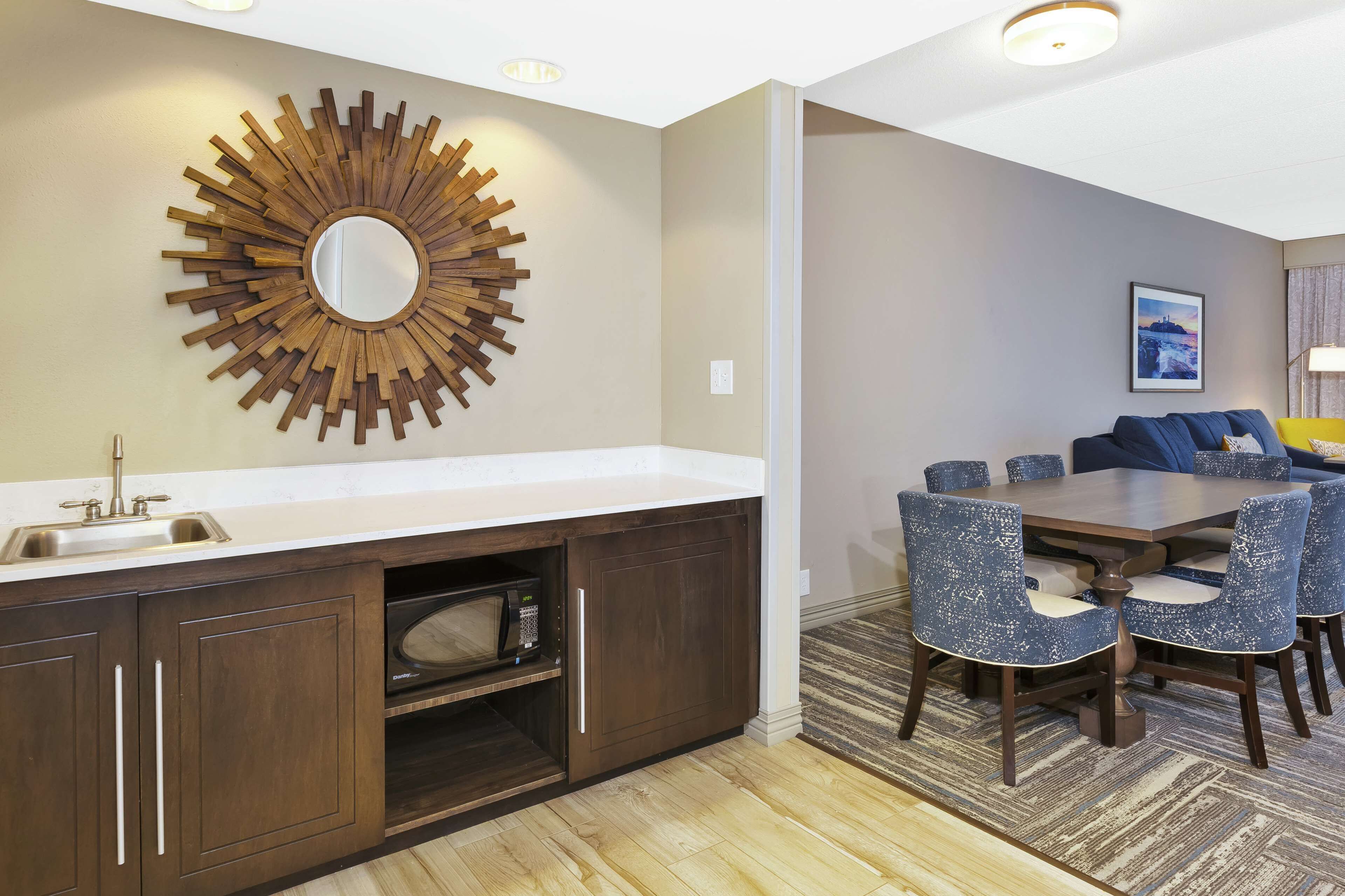A modern kitchen with a built-in microwave, a sink, and a decorative sunburst mirror.
