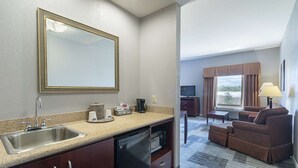 A compact hotel room with a kitchenette, a dining area, and a seating area with a sofa and a TV.