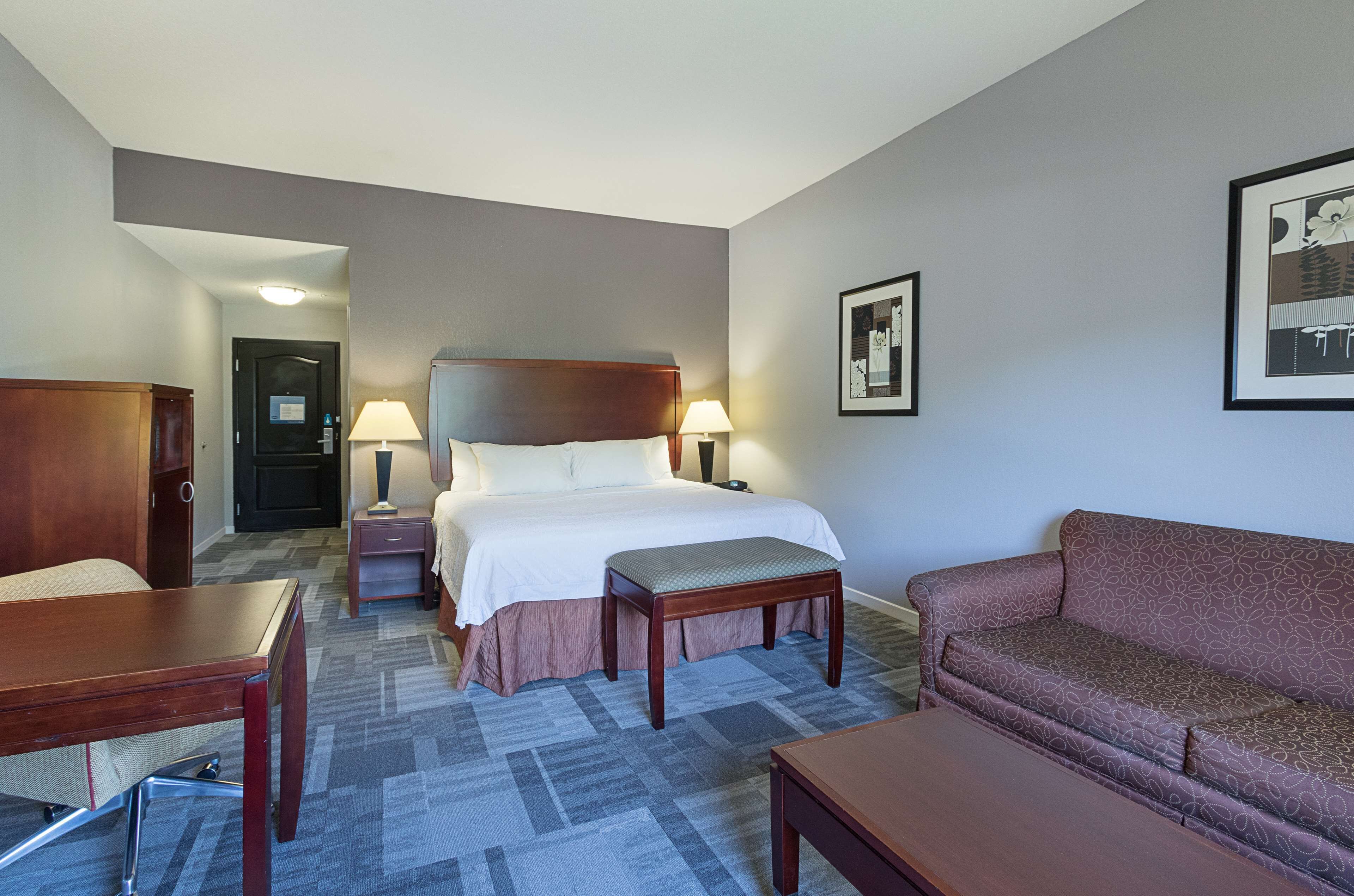 A hotel room with a bed, bedside tables, a sofa, and a desk.