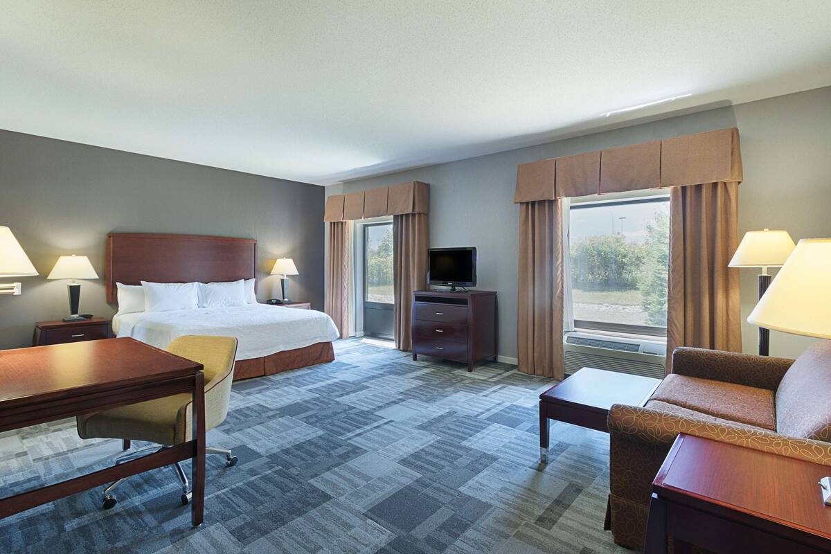A hotel room with a bed, desk, chair, TV, and two lamps.