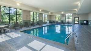 An indoor swimming pool with clear views through large windows, tiled flooring, and several lounge chairs.