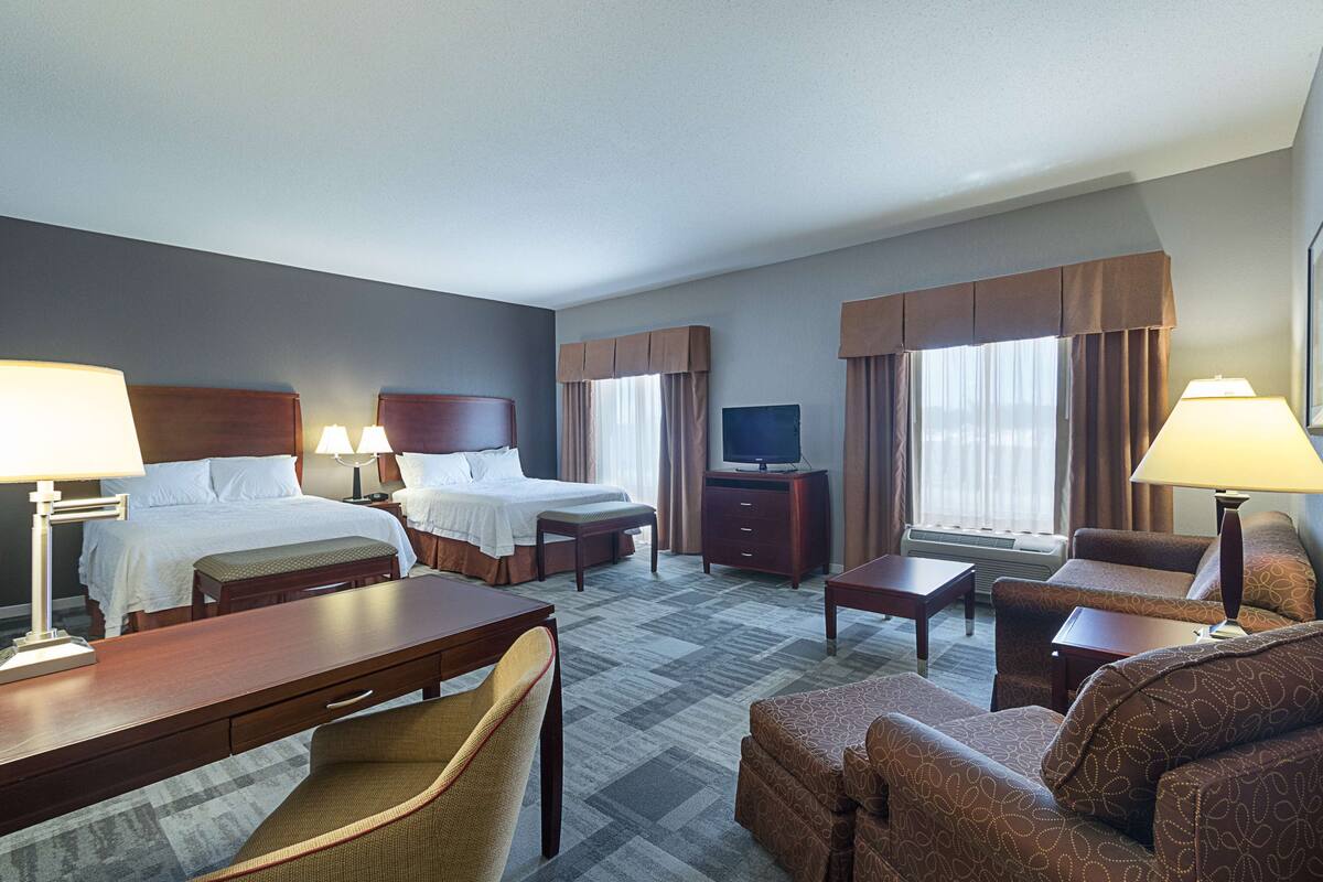 A hotel room with two beds, a TV, a desk, a chair, and a sofa.