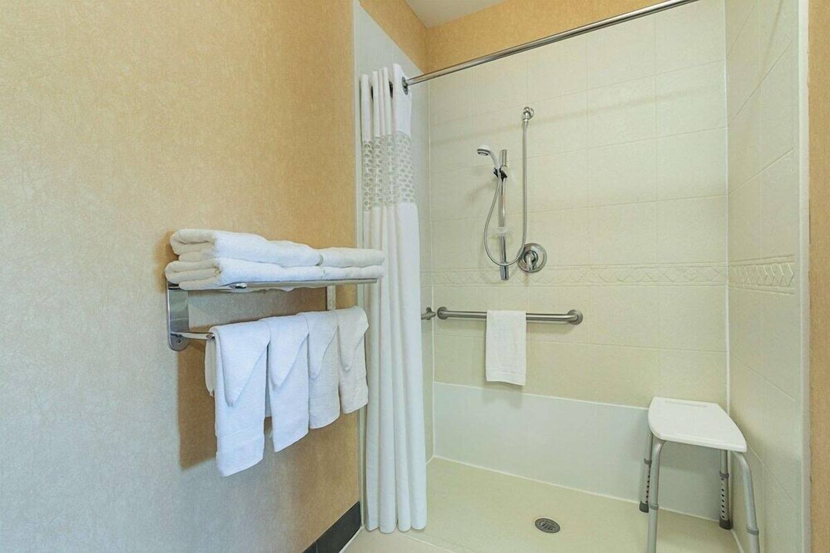 A shower with a handheld showerhead, a towel rack with folded towels, and a small white stool.