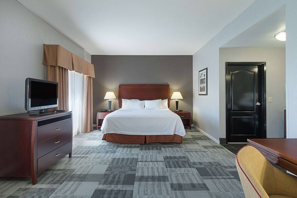 A hotel room with a bed, a TV on a dresser, two bedside lamps, and a door.