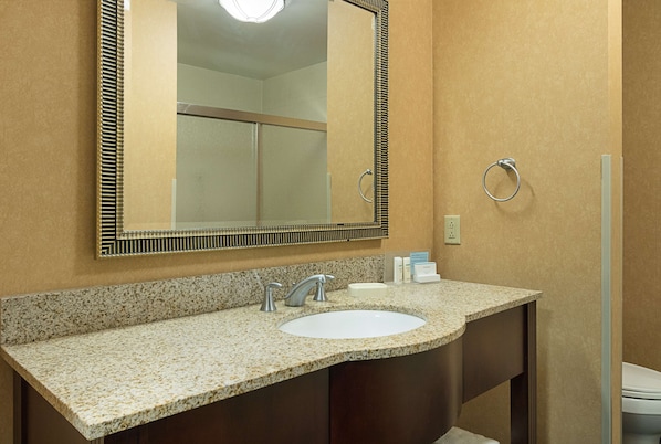 Un baño con lavamanos de encimera de granito, un espejo grande y un aro para toallas.