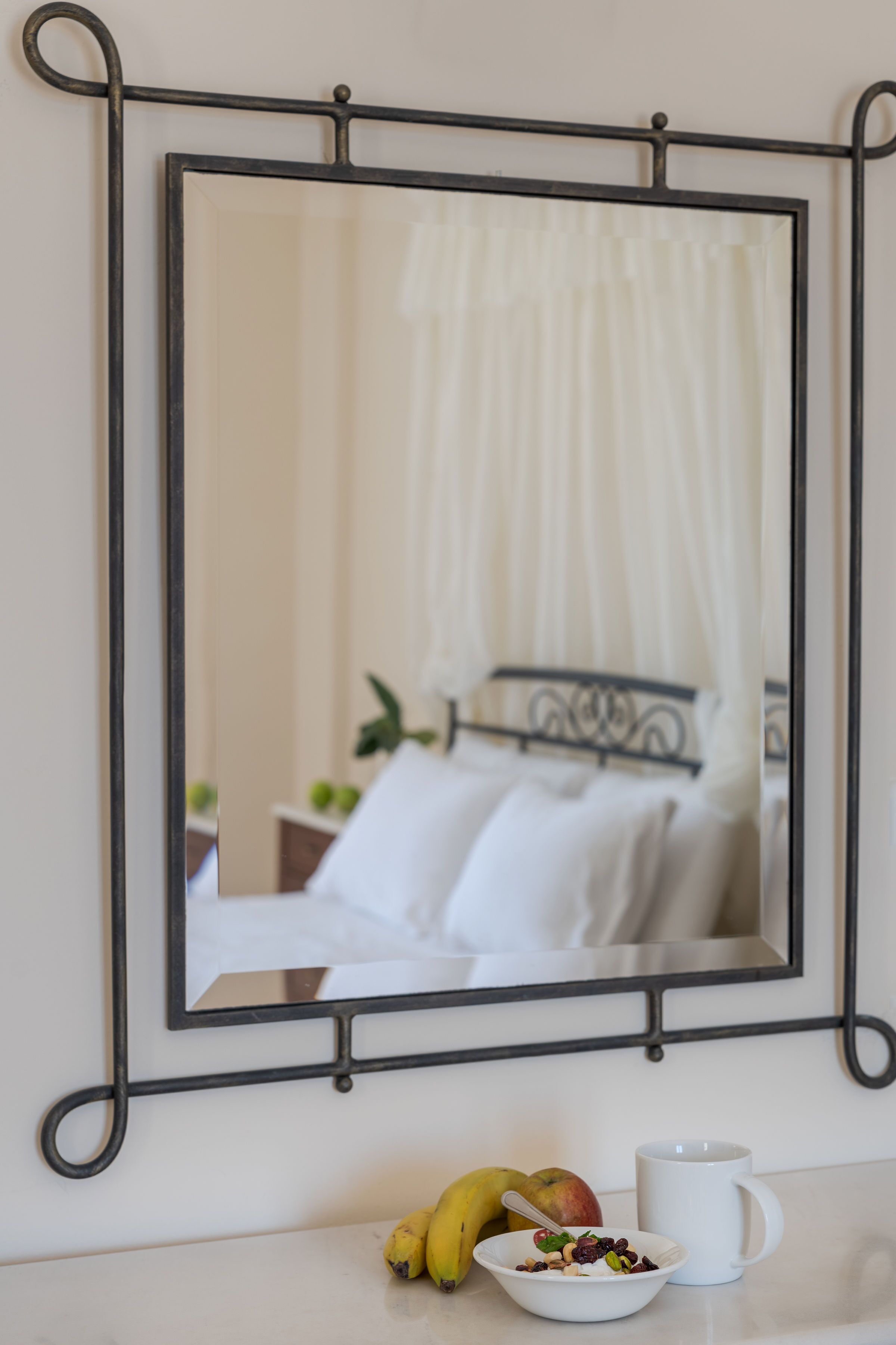 A mirror with a black frame, a bowl of cereal, a banana, and a mug on a white countertop.