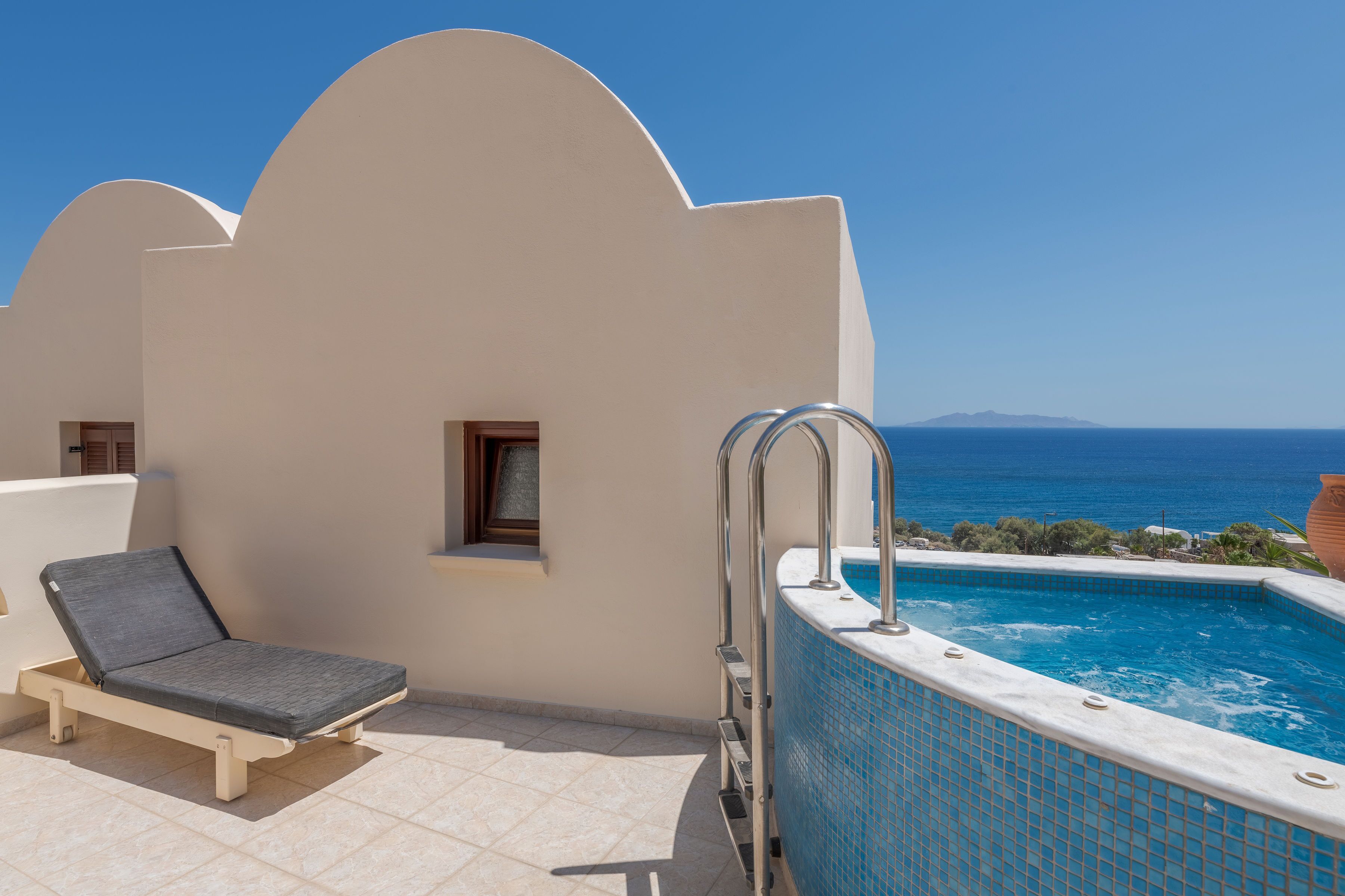 Una tumbona junto a una piscina con vistas despejadas al mar y una montaña a lo lejos.