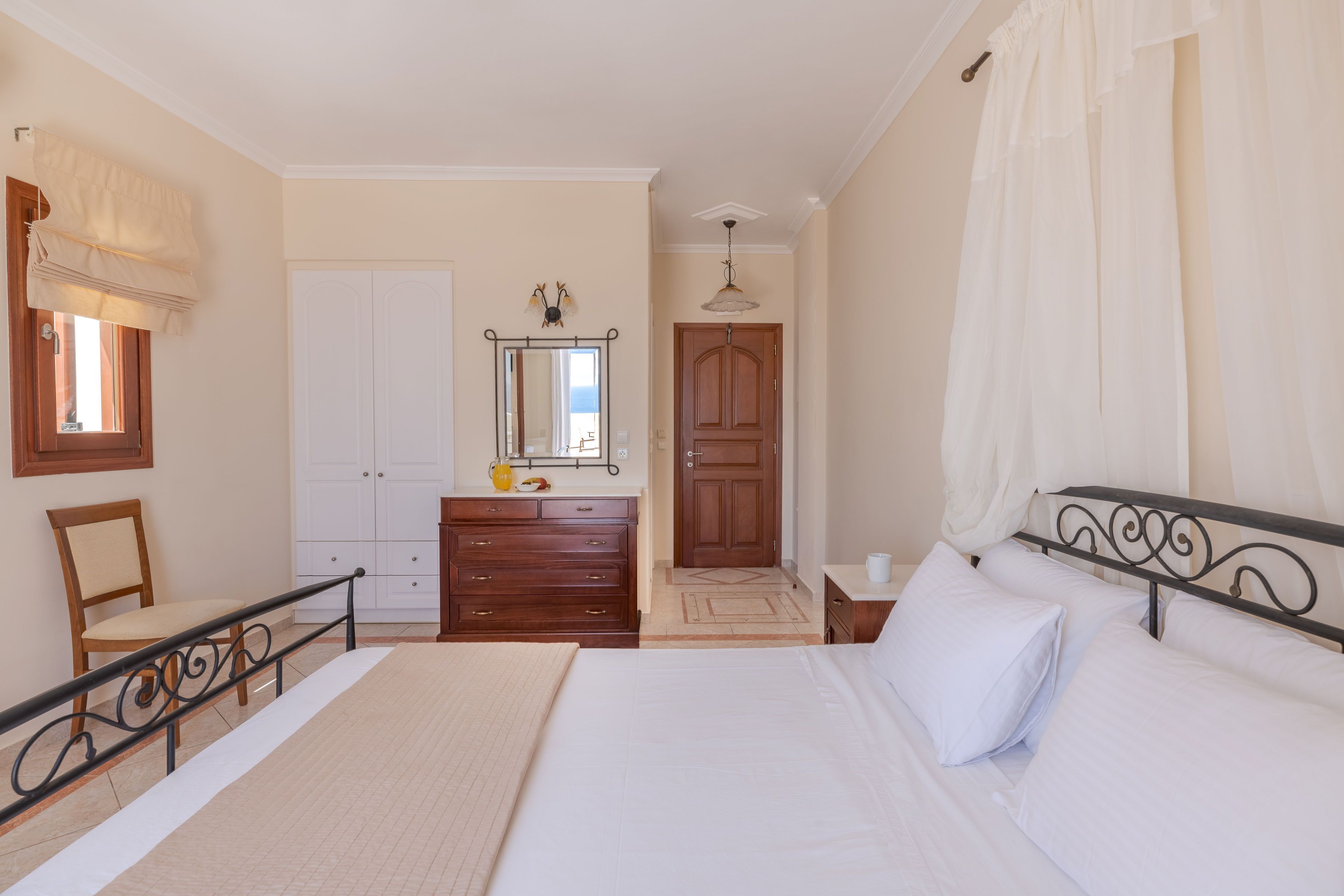Een slaapkamer met een groot bed, een houten dressoir, een spiegel en een deur.
