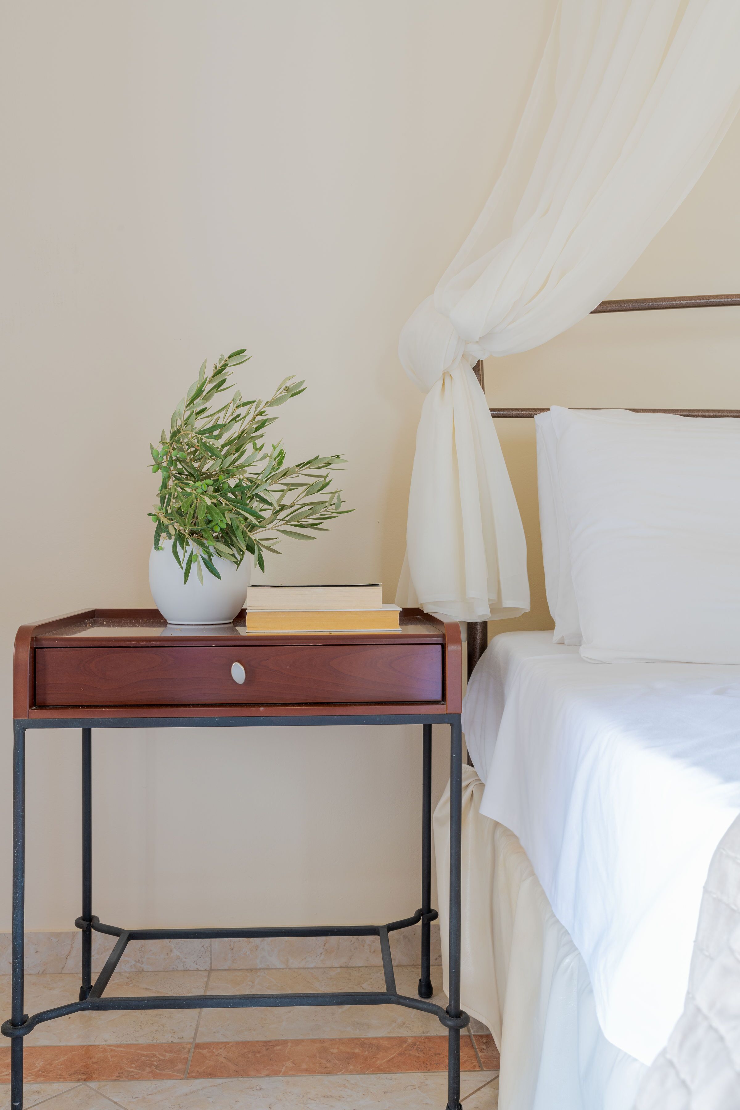 A neatly made bed with white linens, a bedside table with a potted plant, and a book.