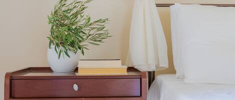 A neatly made bed with white linens, a bedside table with a potted plant, and a book.