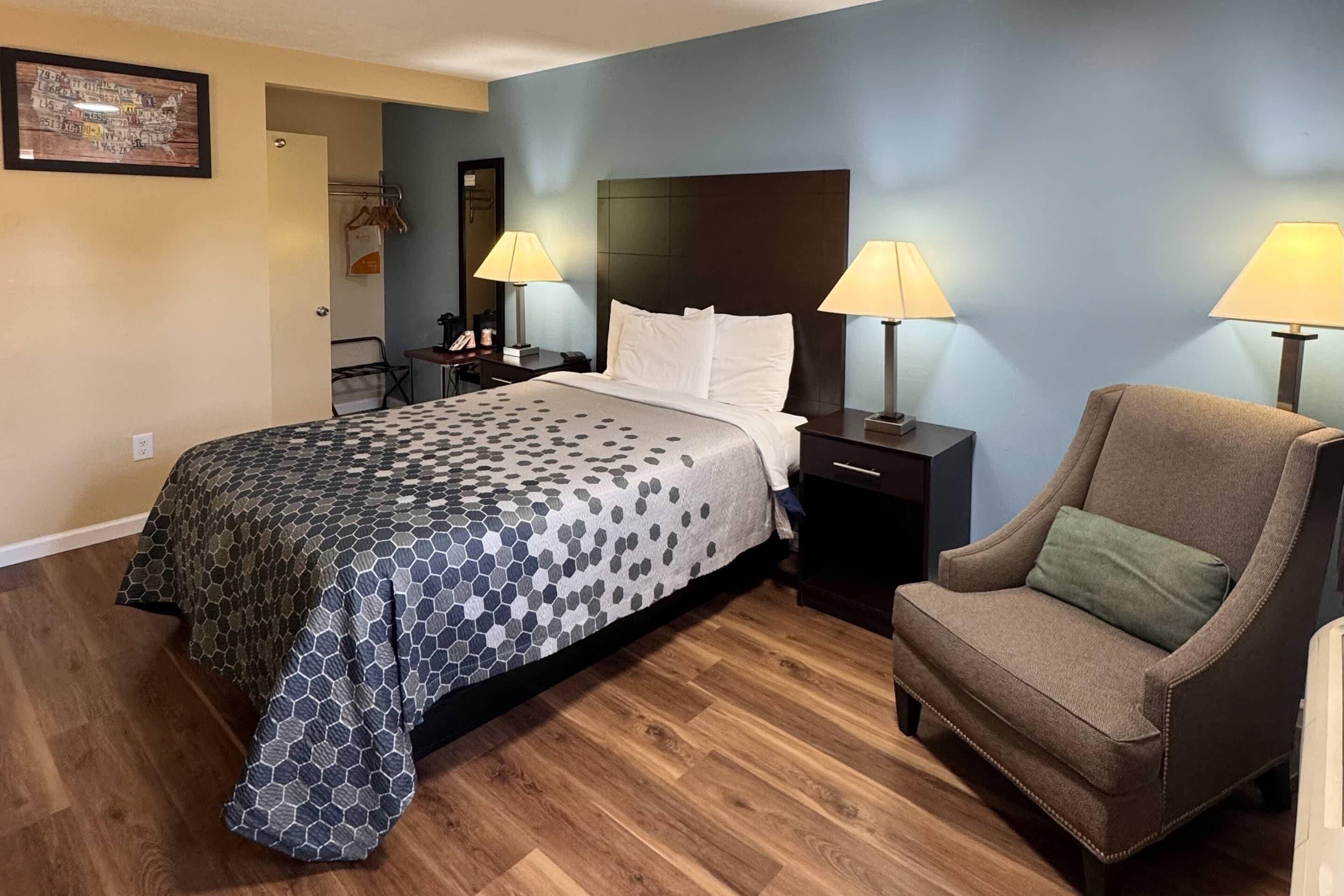 Habitación de hotel con cama, dos lámparas de noche, una silla, mesita de noche y puerta que da a un baño.