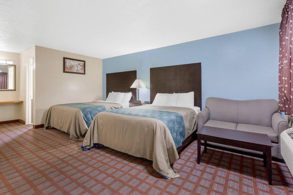 Ein Hotelzimmer mit zwei Betten, einem Sofa, einem Tisch und einer Lampe.