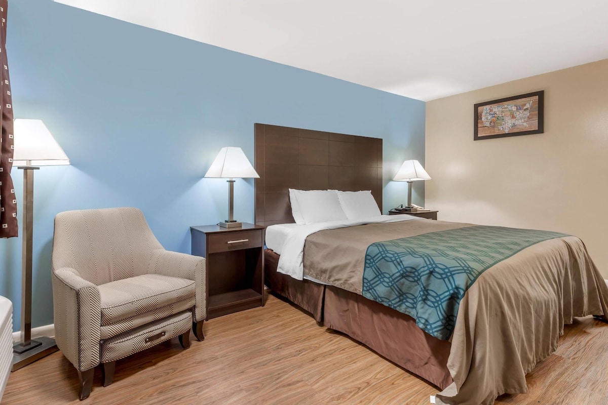 Ein Hotelzimmer mit einem Bett, zwei Nachttischlampen, einem Sessel, einem Nachttisch und einem Wandbild.