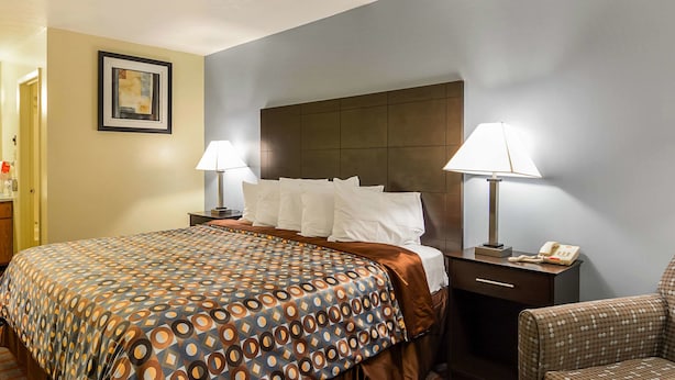 Ein Hotelzimmer mit einem Bett, zwei Nachttischen mit Lampen, einem Sessel und einem gerahmten Bild an der Wand.