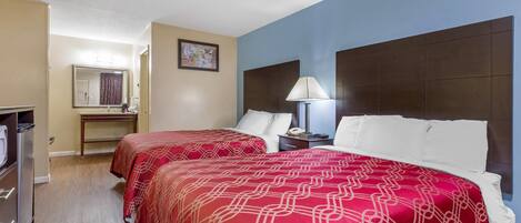 A hotel room with two beds, a desk, a mirror, and a nightstand with a lamp.