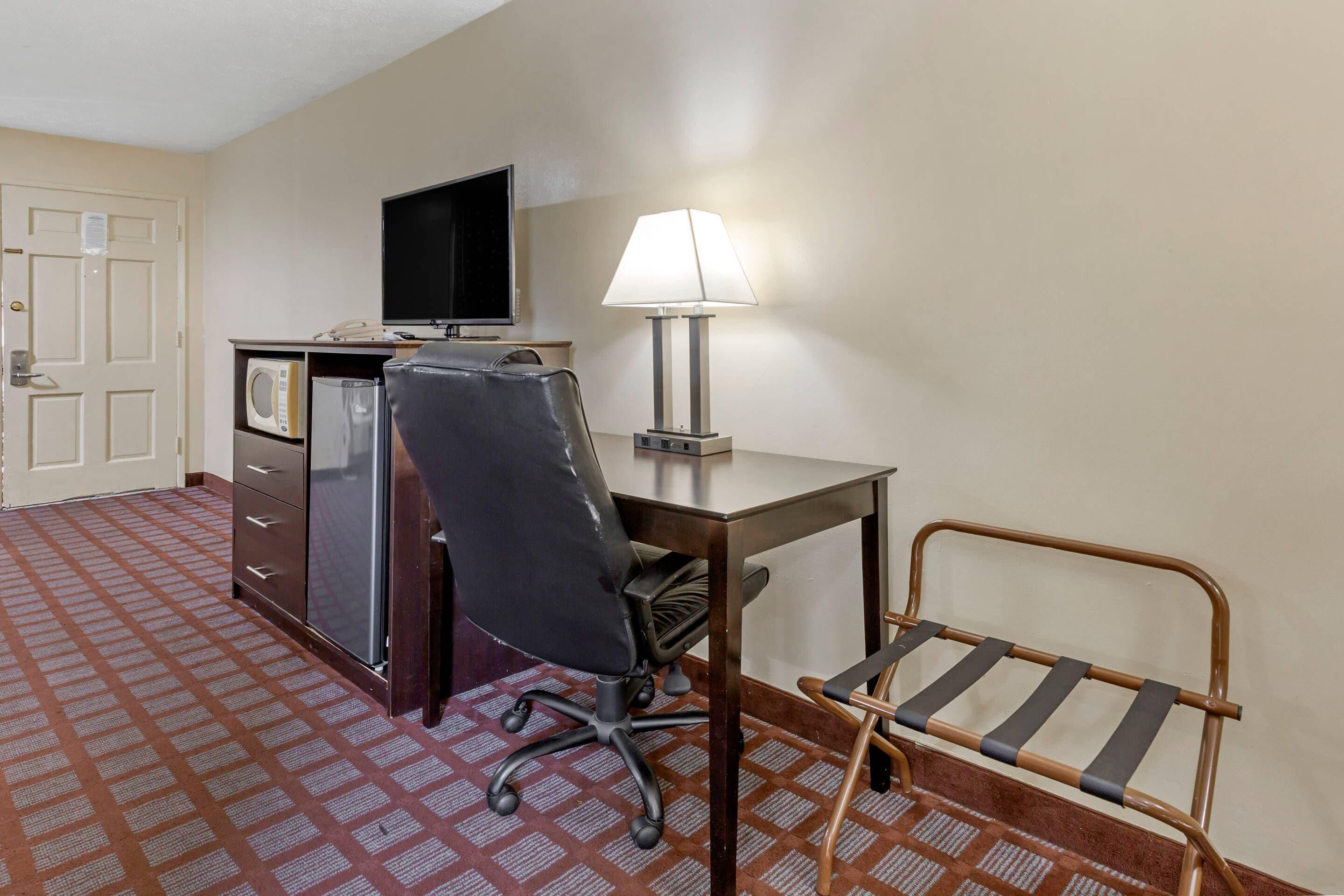 Ein Hotelzimmer mit Schreibtisch, Stuhl, Lampe, Fernseher und einer Minibar.